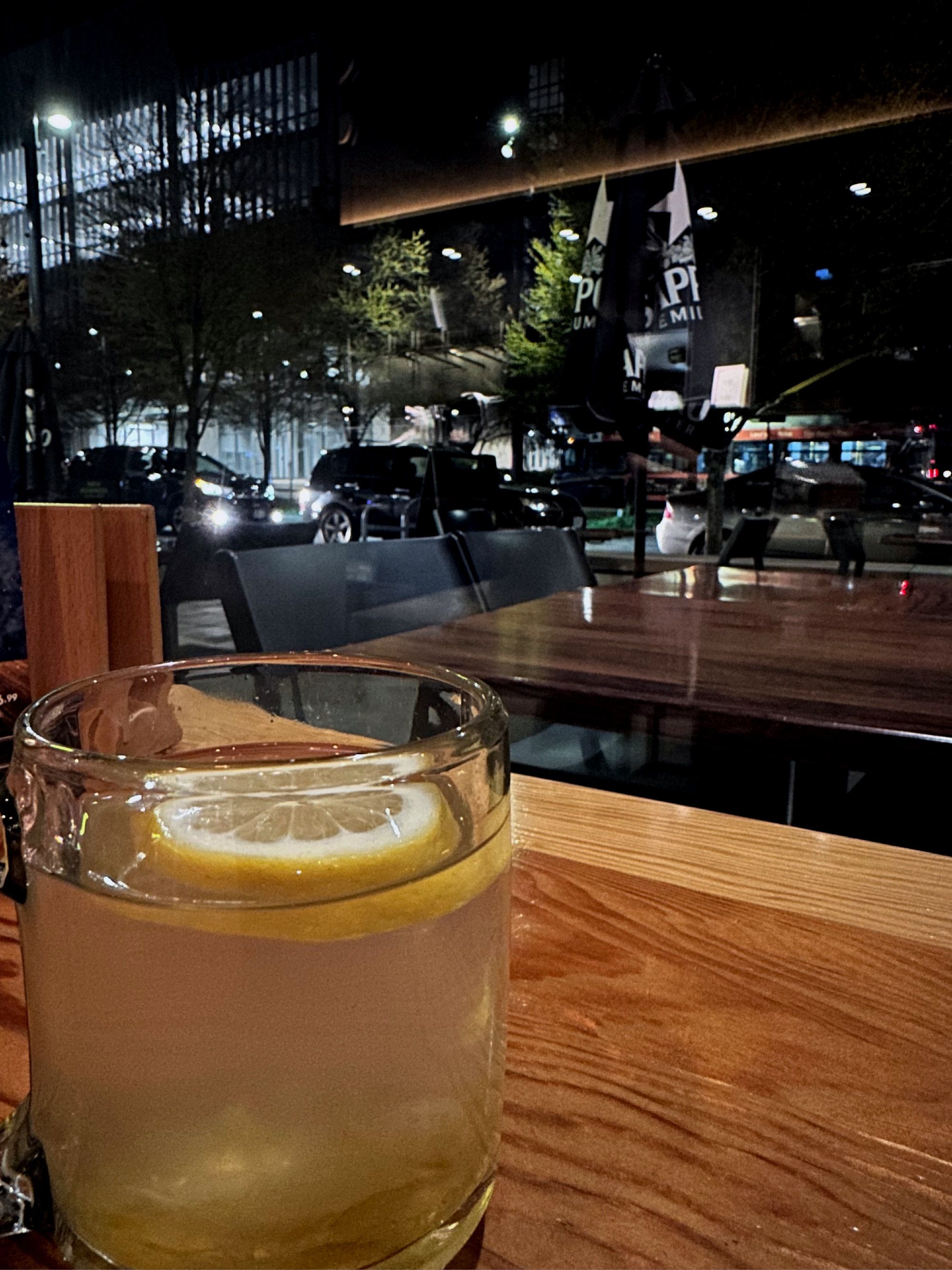 a clear glass with yellow tea and a lemon situated against a night time outdoor dining scene