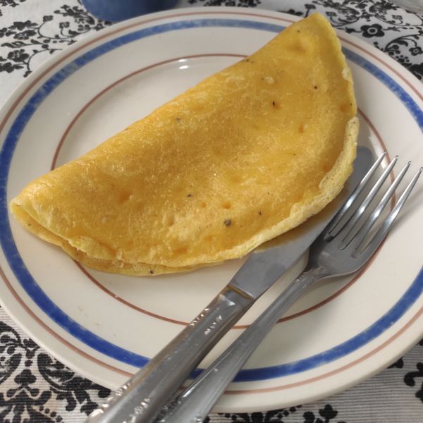 Um pequeno prato, garfo e faca com uma crepioca dobrada, sobre uma mesa.